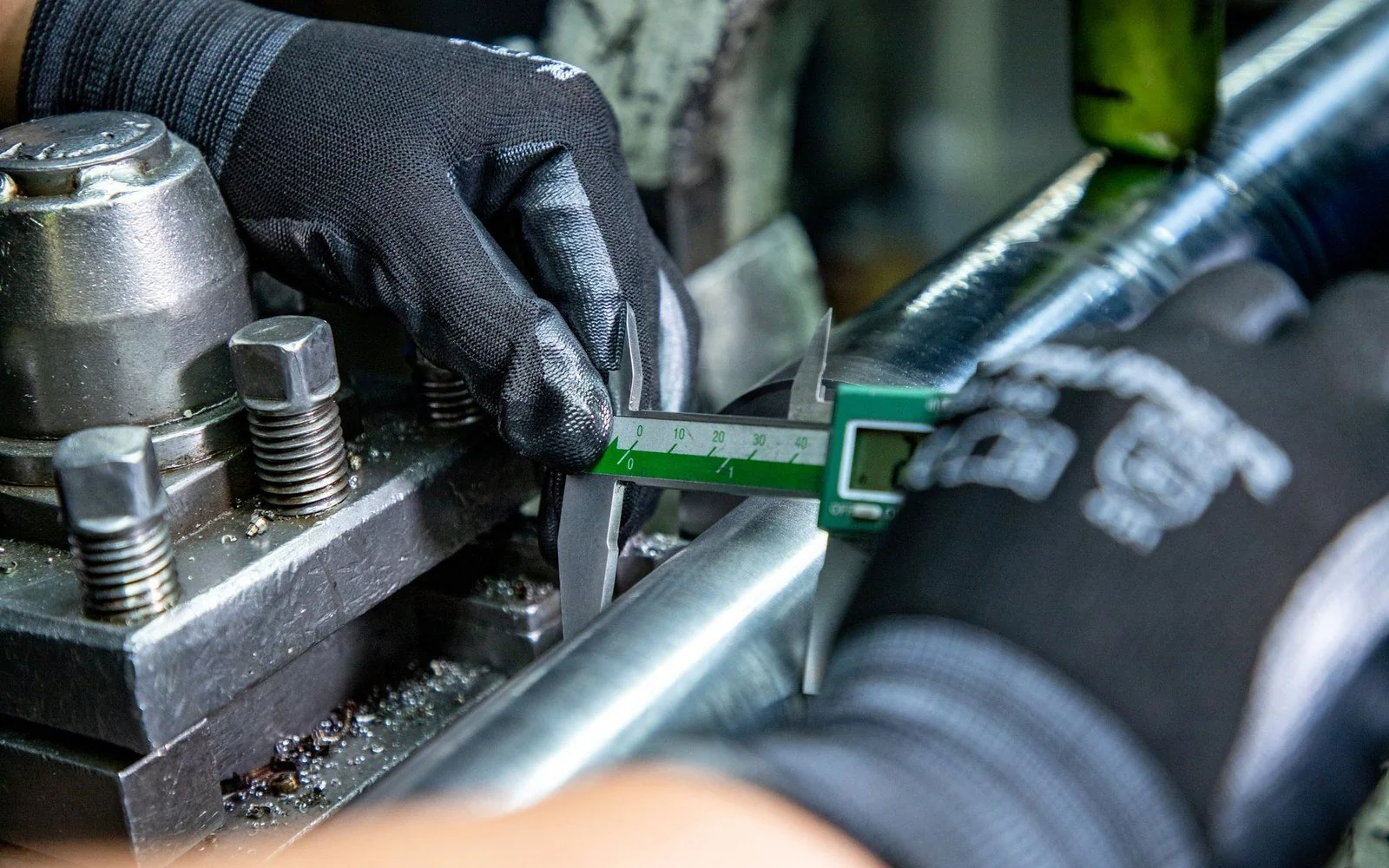 Gloved hands checking a metal component with a digital caliper